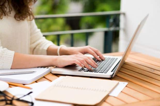 woman writing at laptop with a pen and paper on table