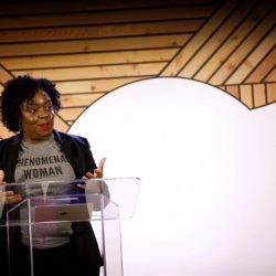 Kimberly Bryant stands behind a podium wearing a shirt that read Phenomenal Woman