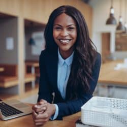Smiling young African American businesswoman leaning on a table in her office