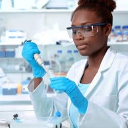 African-american scientist or graduate student in lab coat and protective wear works in modern laboratory