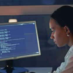 Close up of african american woman working on computer in electronics laboratory. Doing Development of Software and Hardware. She wearing a lab coat. Side view