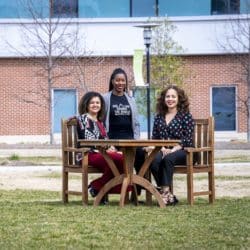 three black women nuclear engineers seated at table on the grass outside office building