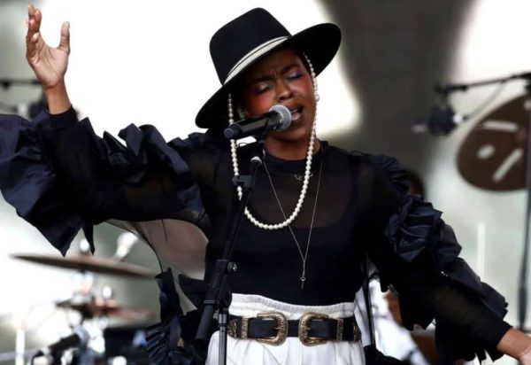 Lauryn Hill singing on stage wearing a black hat with pearls