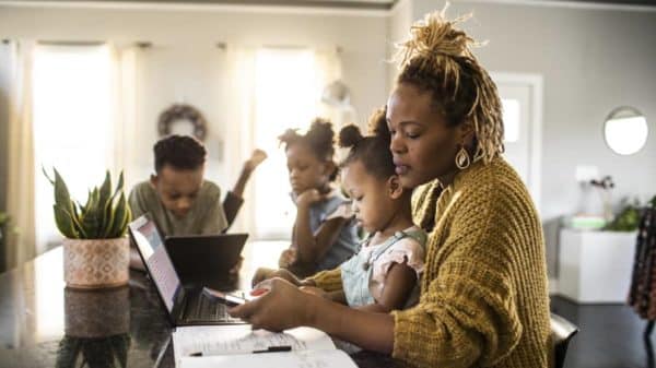 Woman working from home at her kitchen counter while her three kids surround her