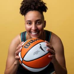 Trans athlete for the WBNA posing for a portrait image while holding a basketball up to the camera smiling